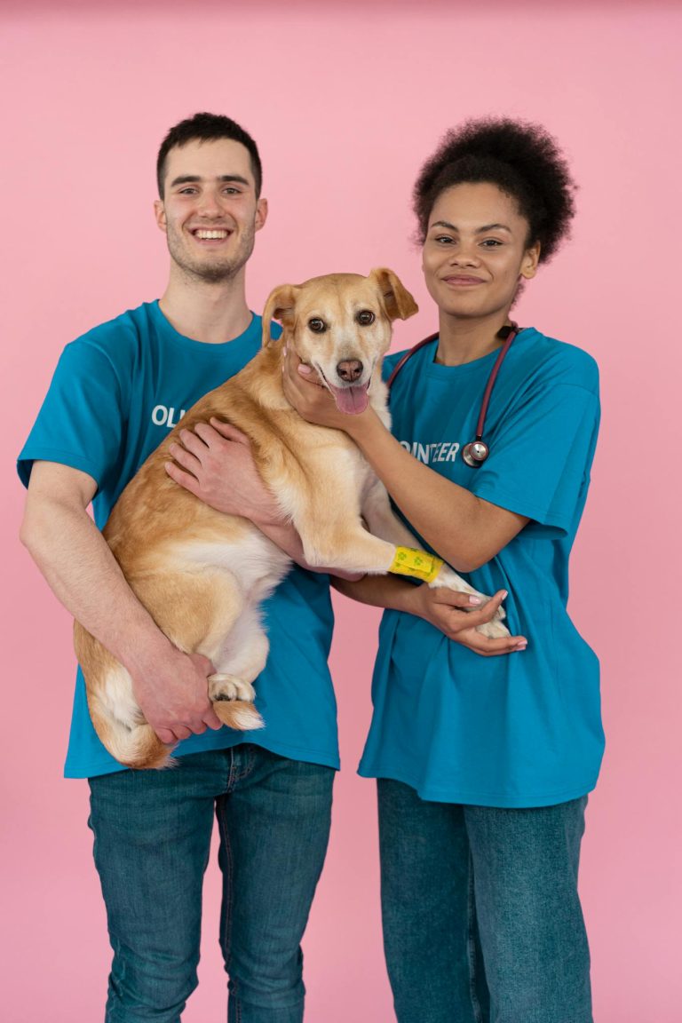 Two smiling volunteers holding a friendly dog, showcasing adoption spirit.